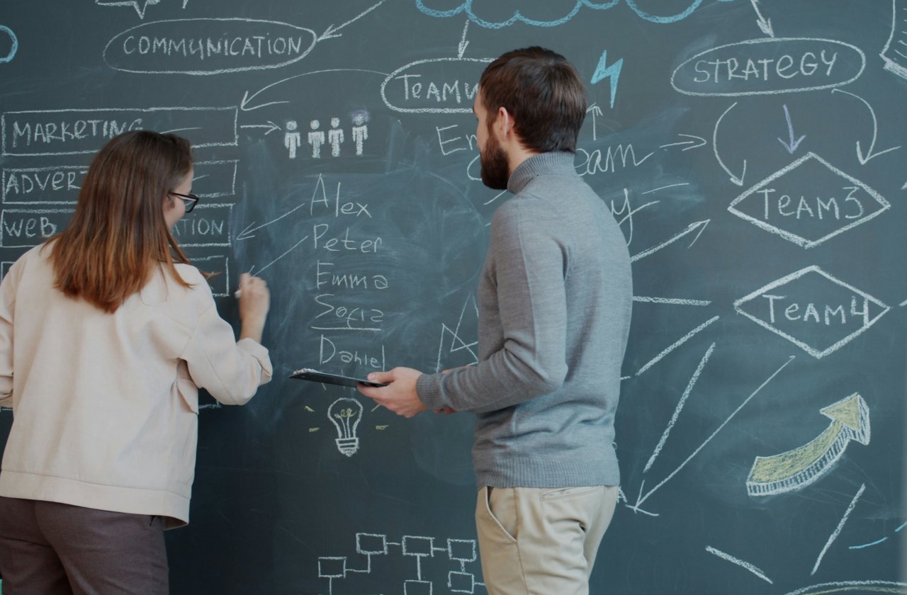 Two colleagues mapping a team structure on a chalkboard.